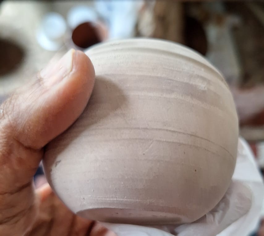 A newly thrown ceramic pot held gently in one hand