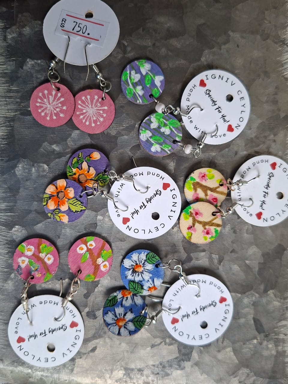 Many pairs of hand painted wooden disc earrings laid out on a metal surface