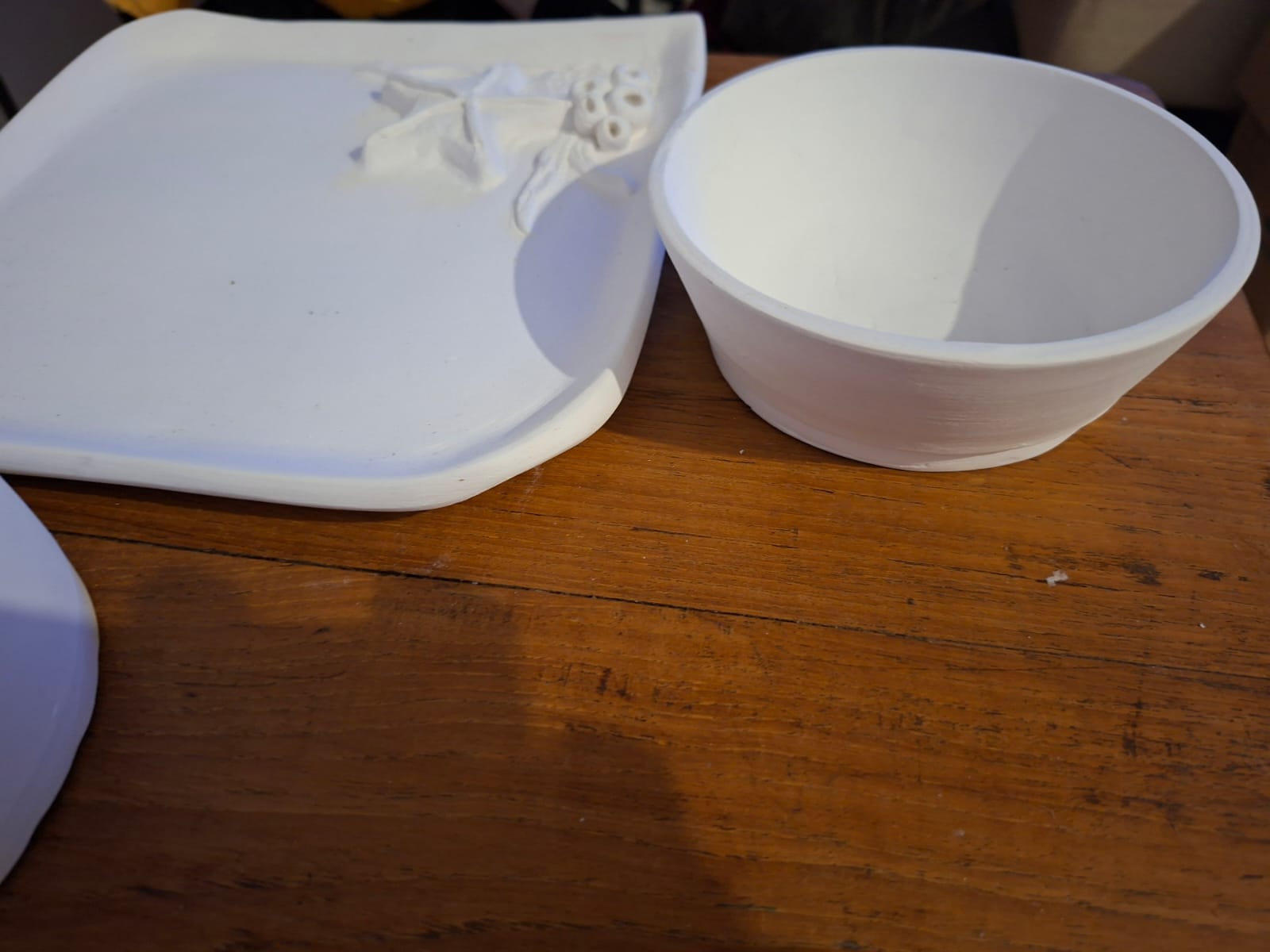 An unglazed bowl and relief decorated tray waiting on a worn wooden table