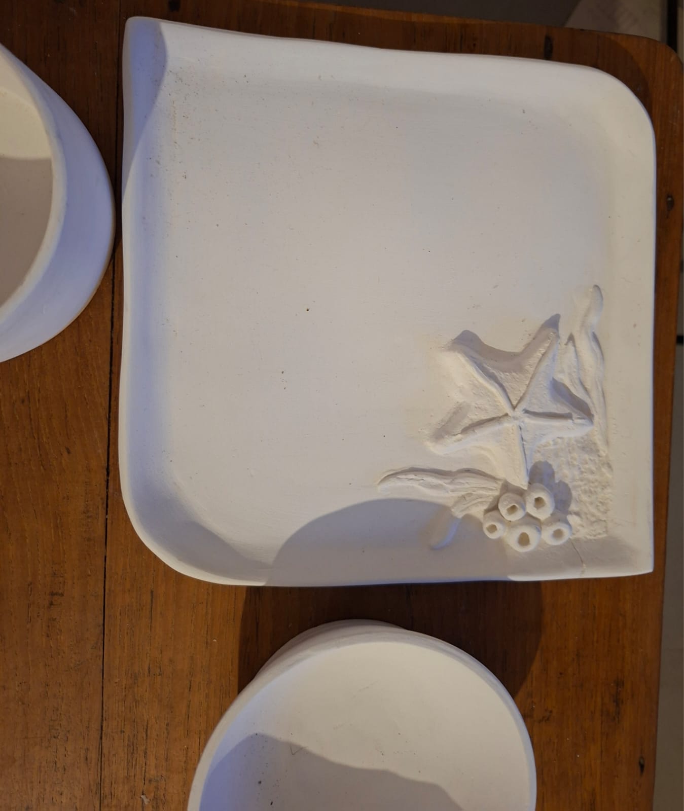 An unglazed square clay tray with a starfish and coral relief in one corner