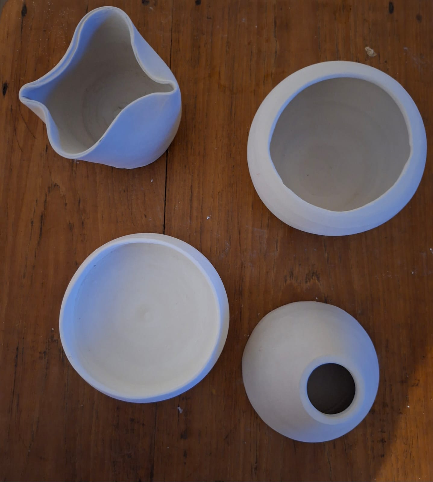 Four unglazed stoneware vessels on a wooden table, seen from above