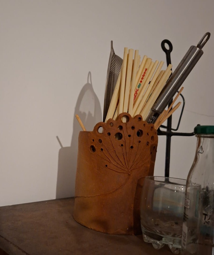 Handmade red clay dandelion pen pot in use on a work desk