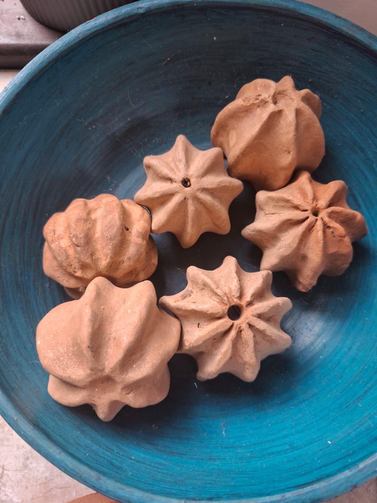 Moulded red clay forms resting in a teal fluted bowl
