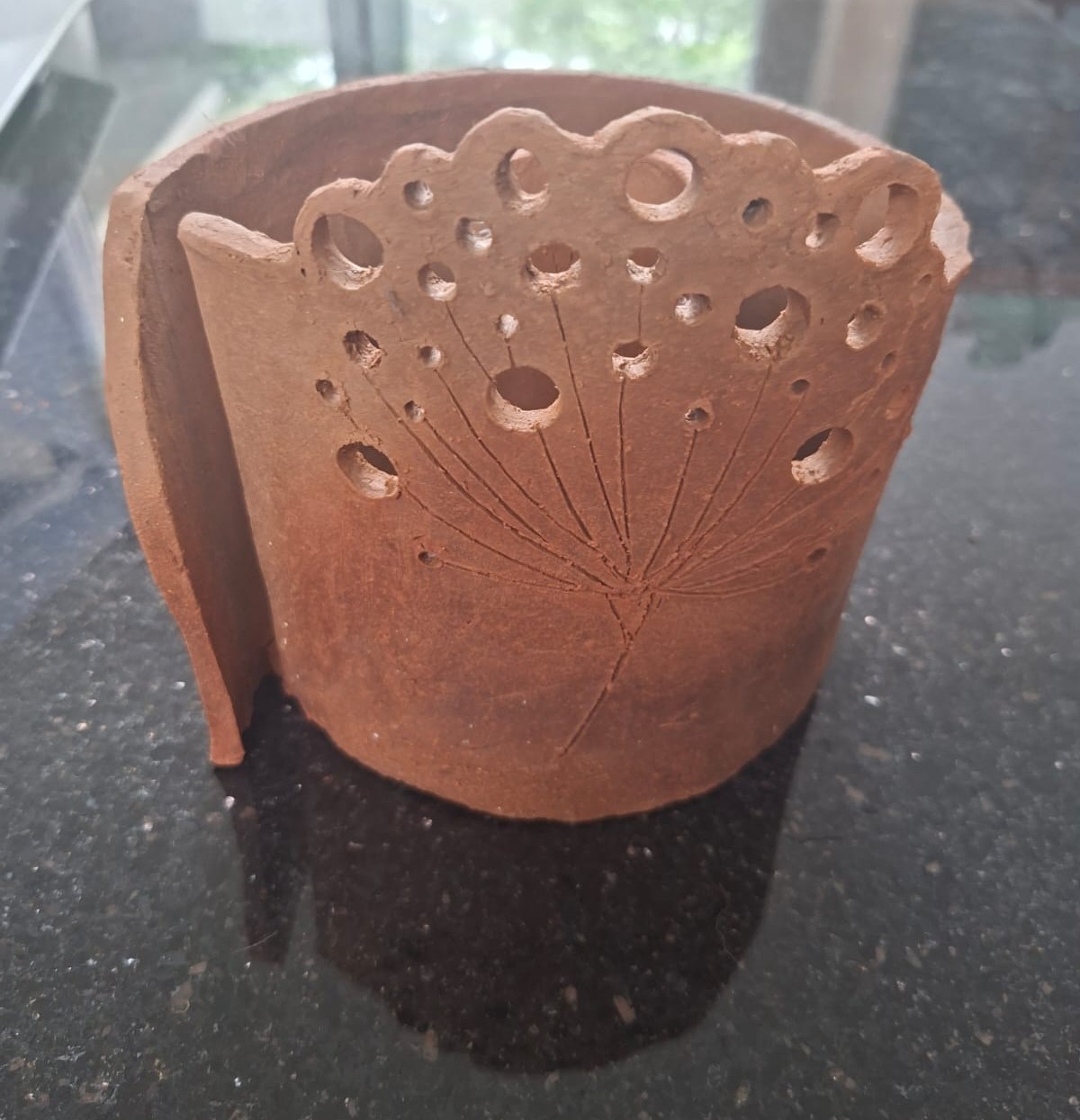 A pierced red clay dandelion pot catching the light