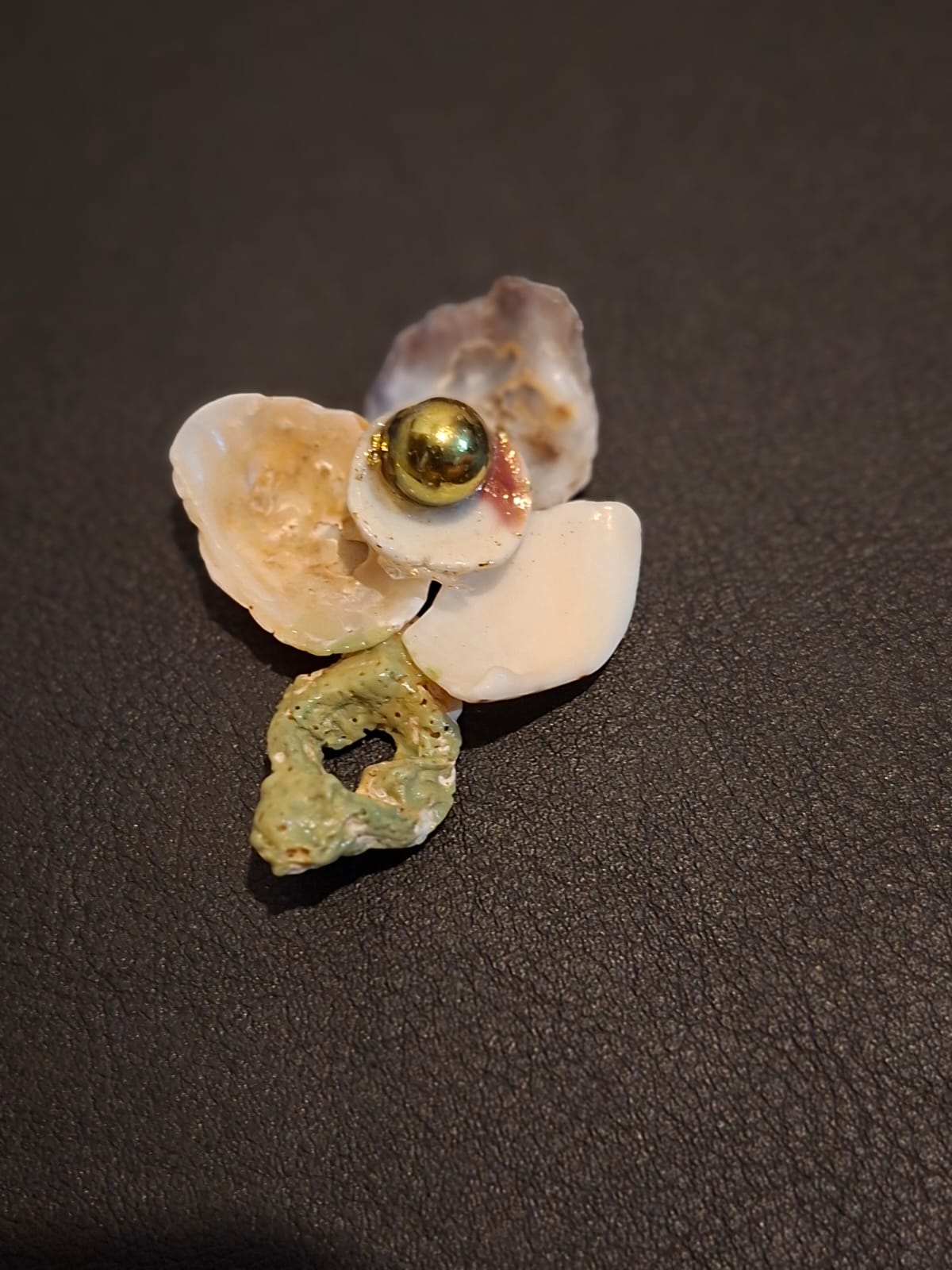 A shell brooch with a golden bead at its centre and a green glazed stem