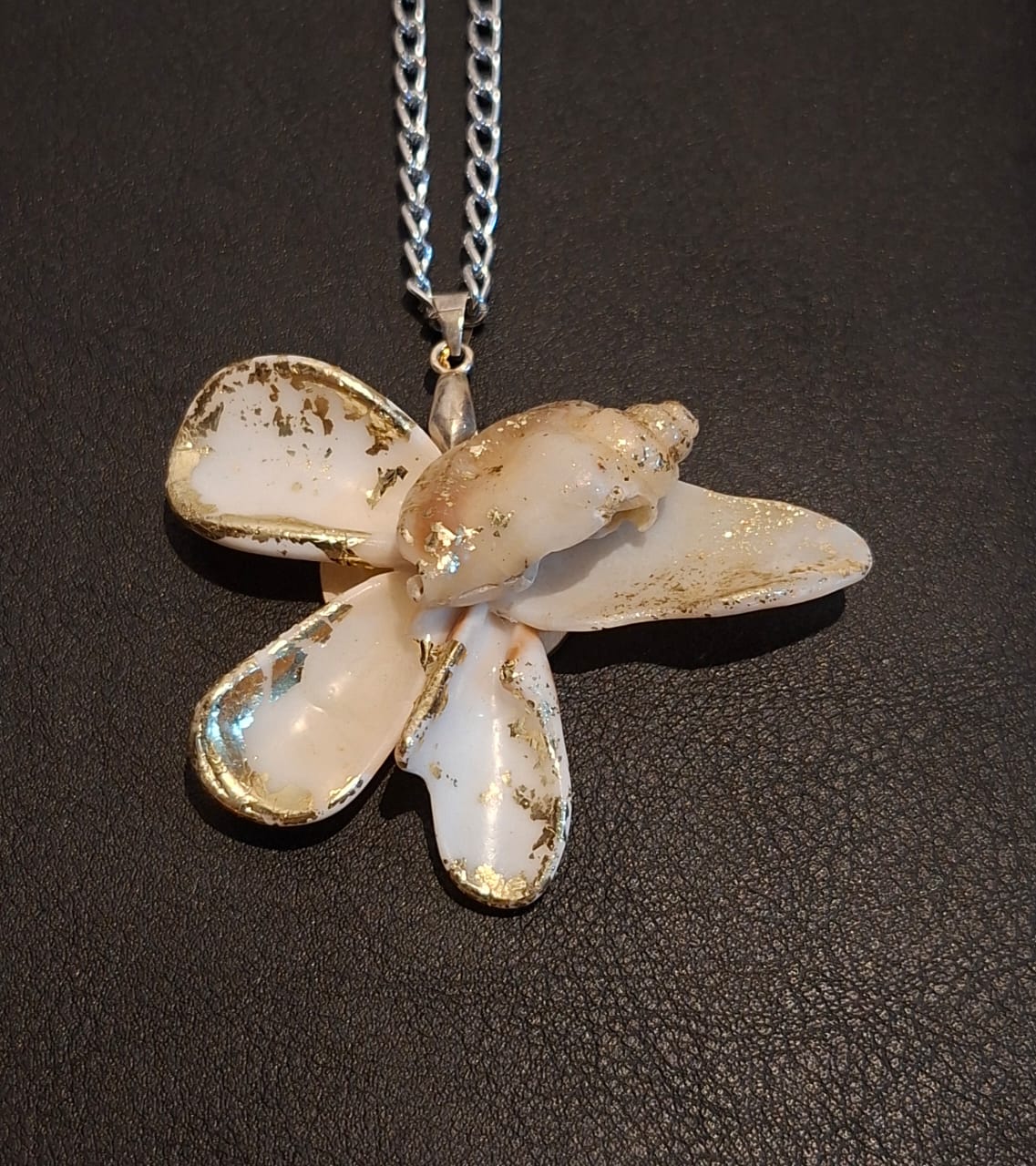 A five petalled shell pendant edged in gold leaf, hanging from a silver chain