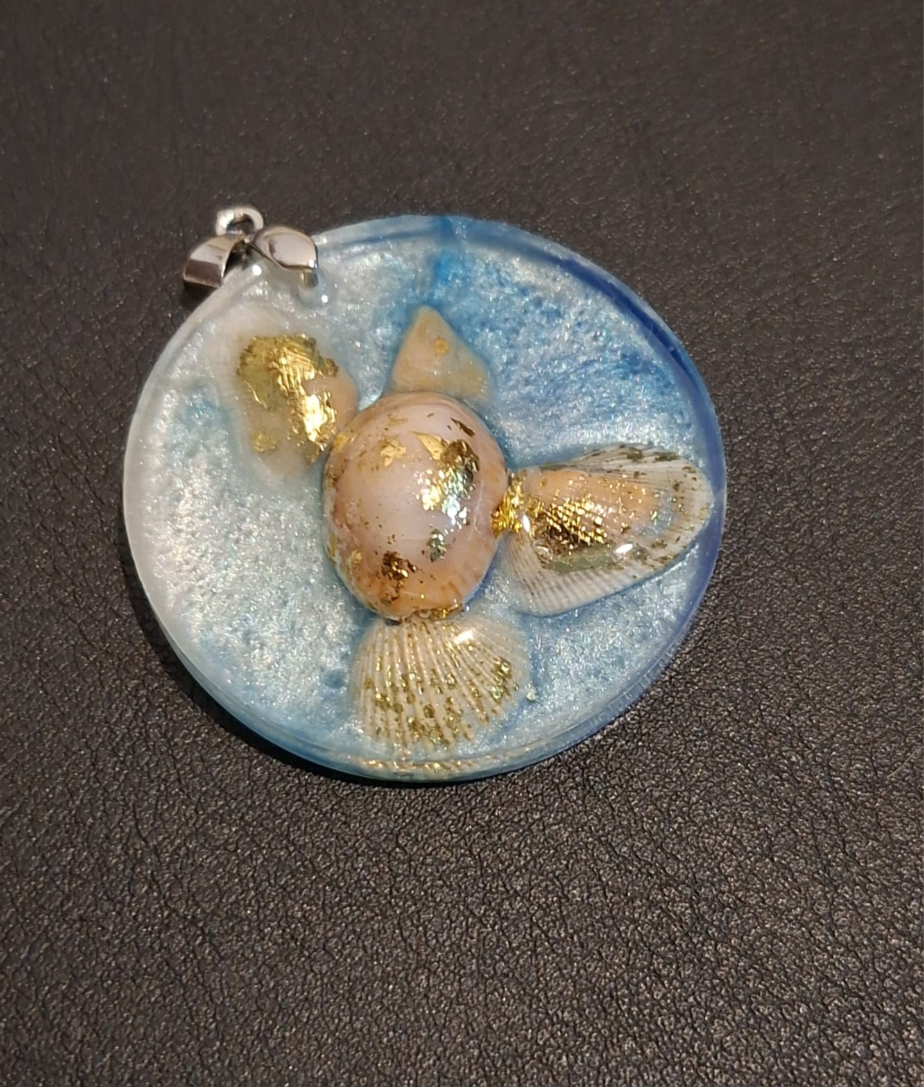 A round pendant of pale blue resin holding shells and gold leaf