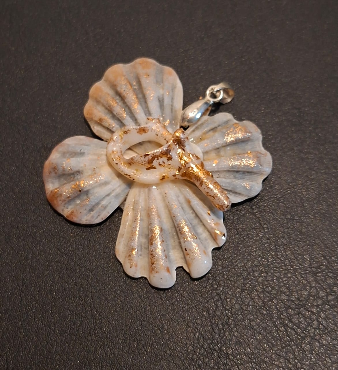 A pendant built from pale scallop shells arranged as a hibiscus, flecked with gold leaf