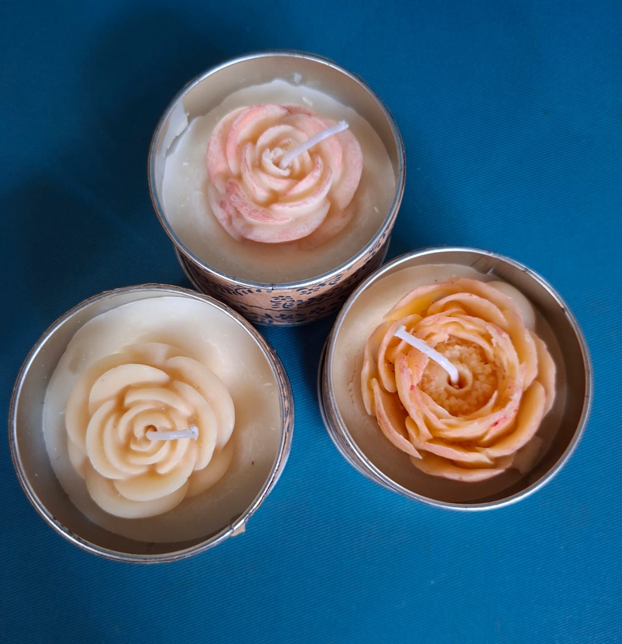 Three tinned candles poured as roses, on a blue cloth