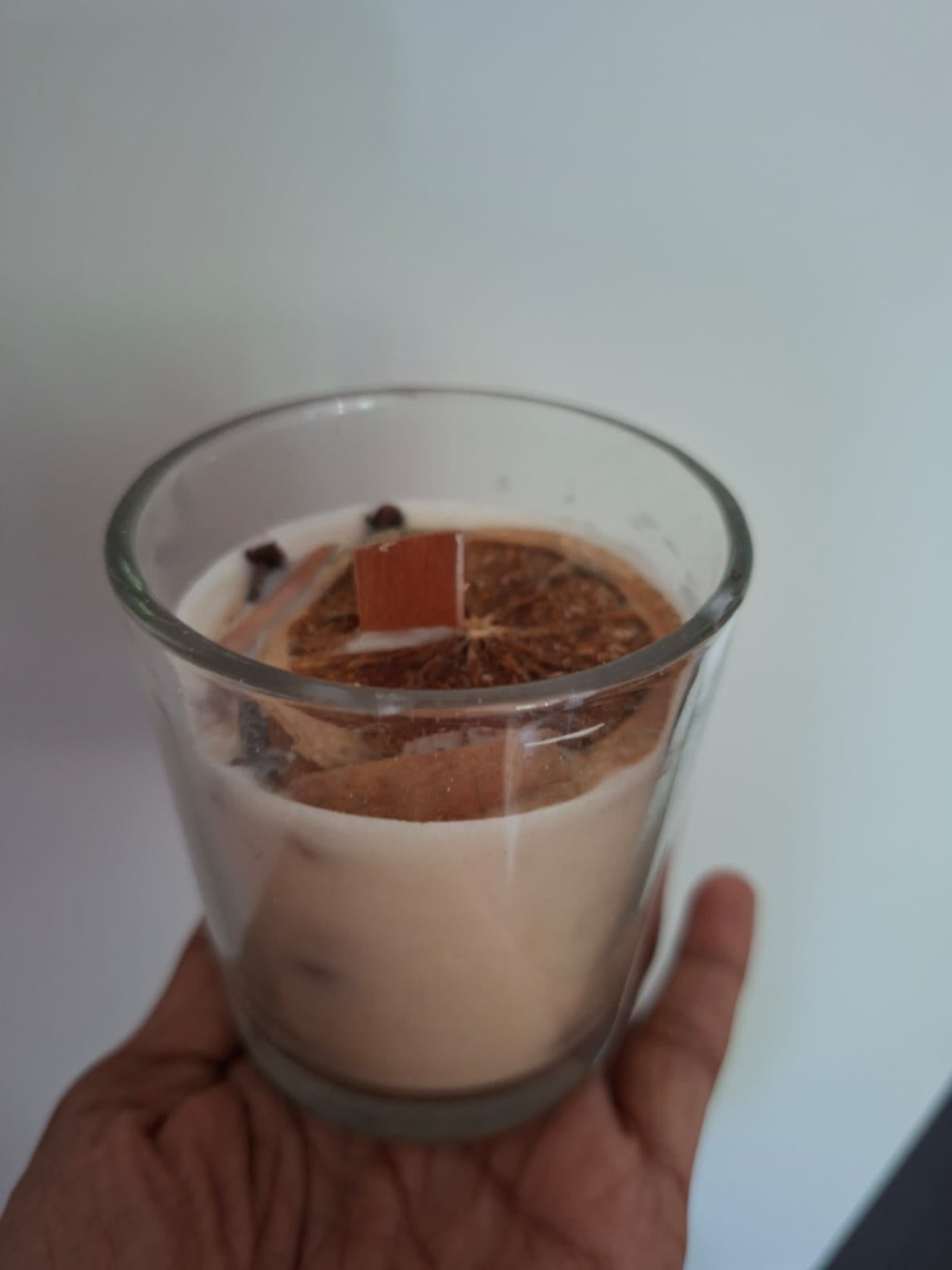 A glass candle topped with dried orange, cinnamon and cloves, held in one hand