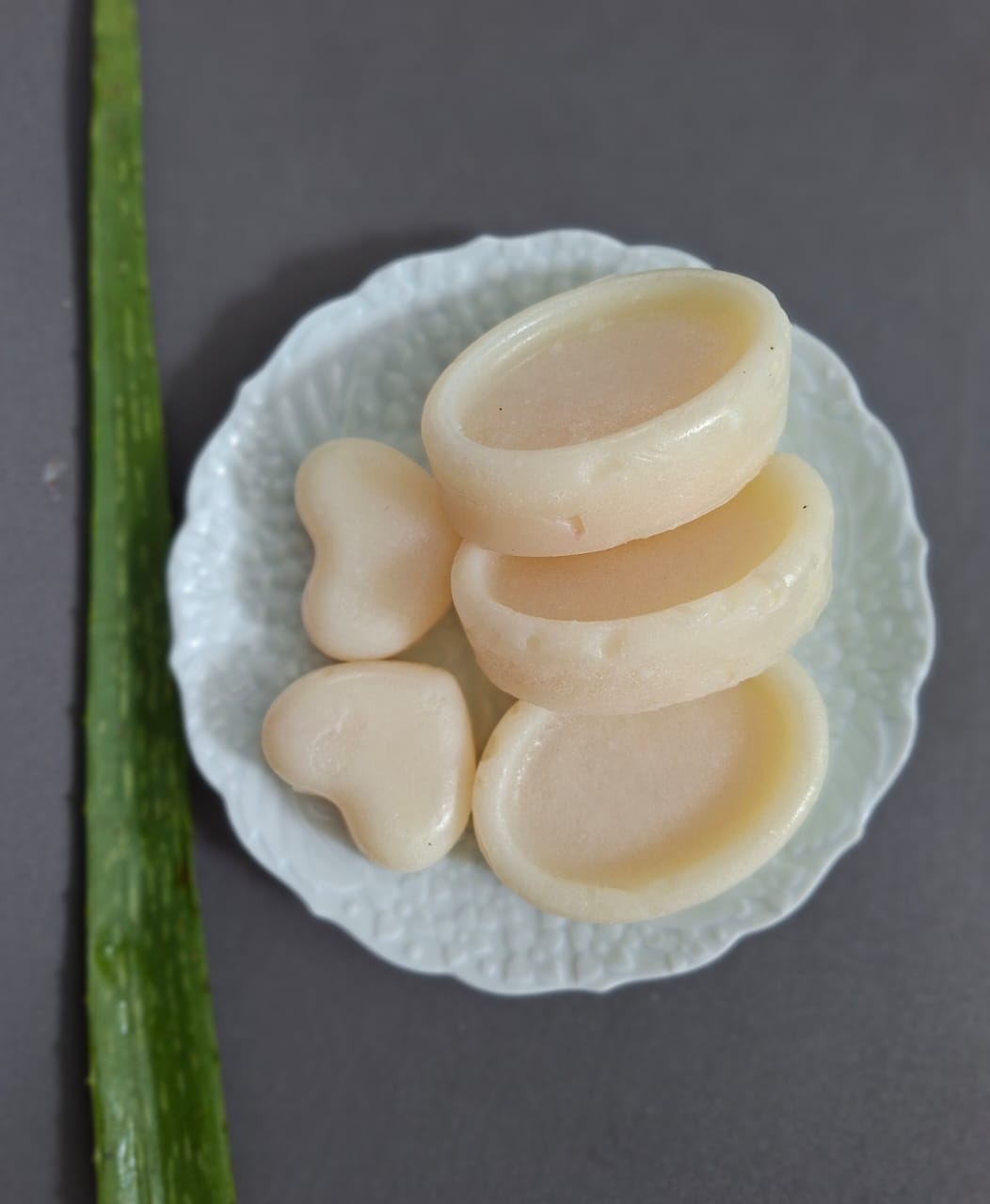 Pale soap rounds and hearts on a white dish beside a cut aloe leaf