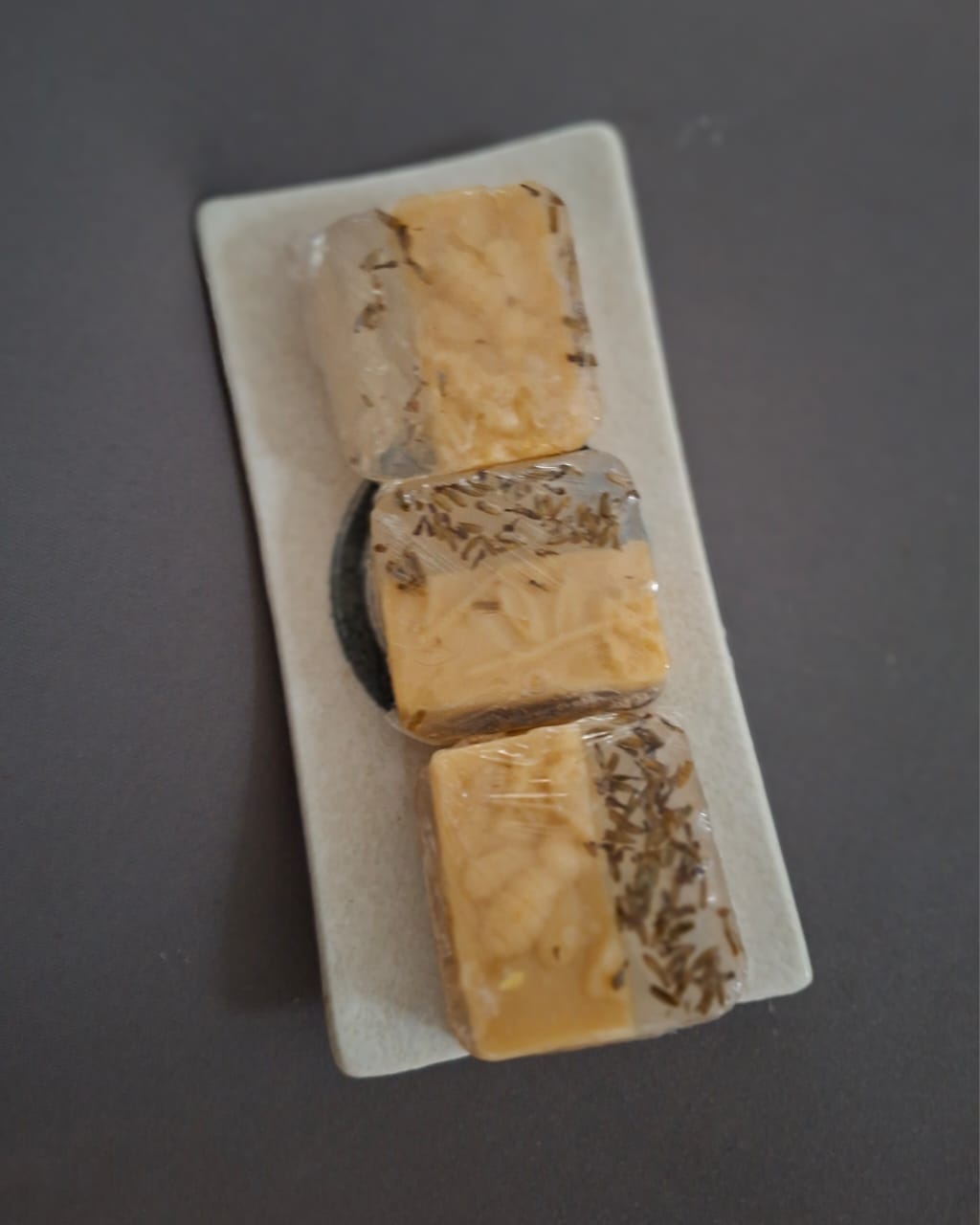 Wrapped soap bars speckled with dried herbs on a cream tray