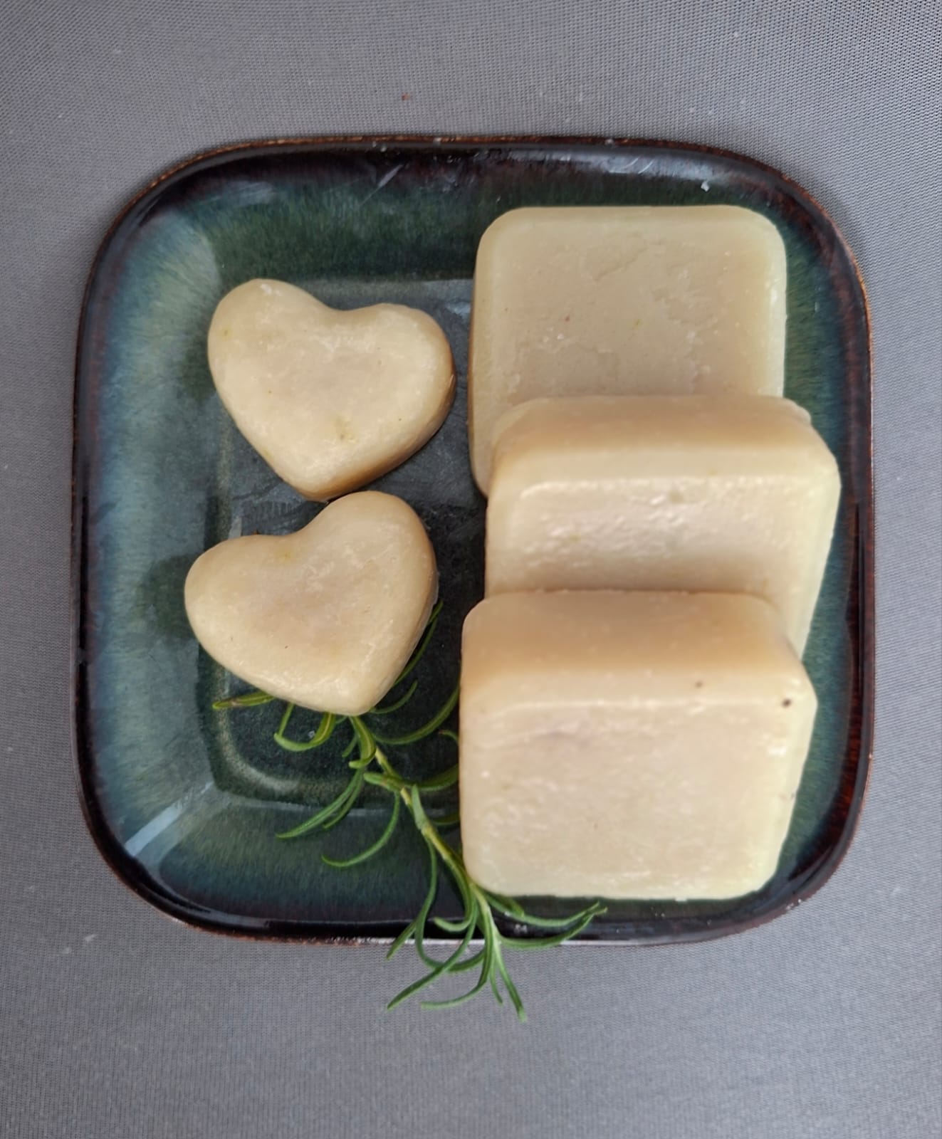 Handmade soap bars and hearts on a green glazed dish with a sprig of rosemary